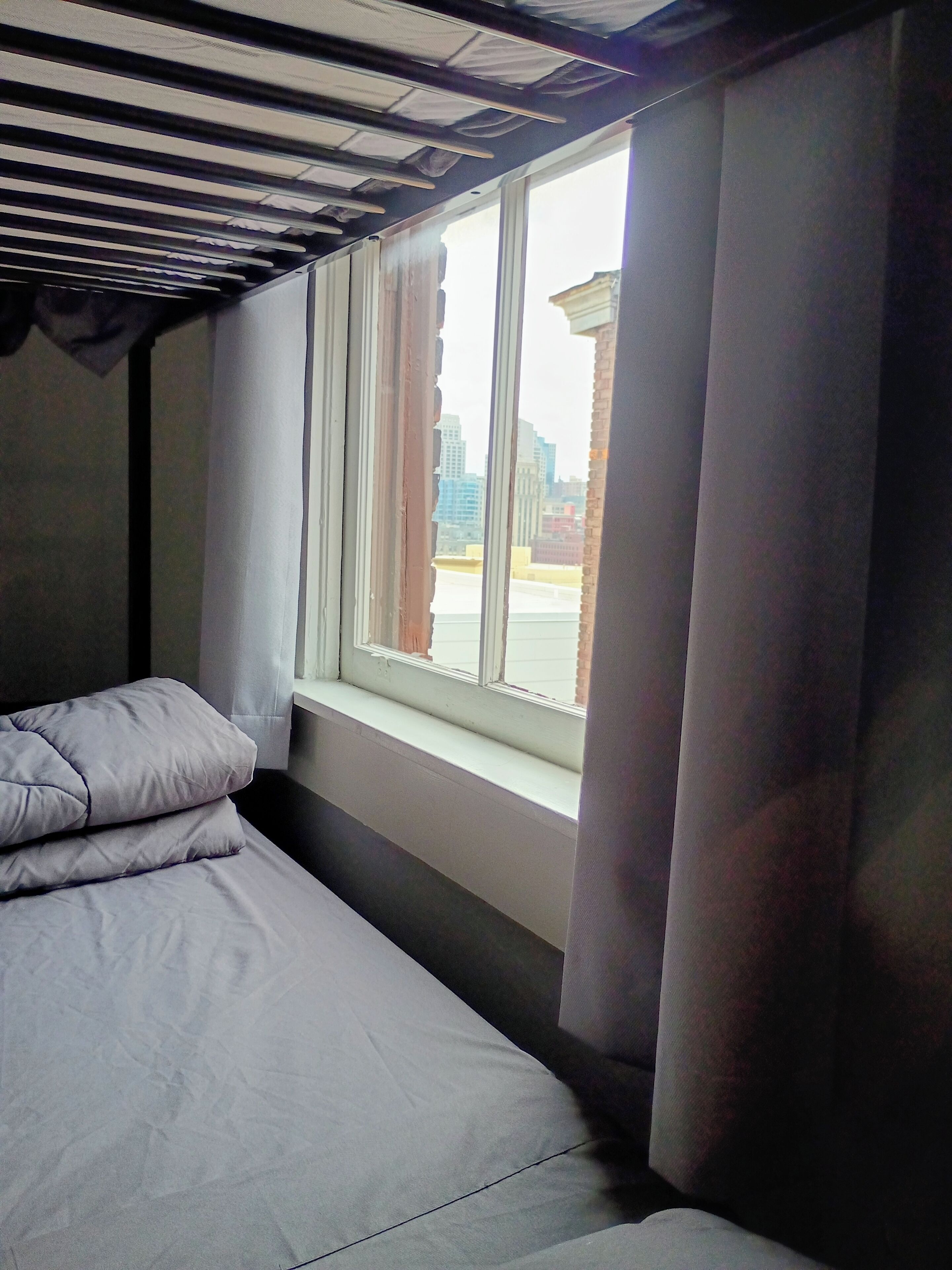 Ein Zimmer mit einem Bett, einem Fenster und Blick auf Gebäude.