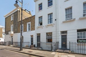 A row of white buildings with multiple windows and a black metal fence in front. - Maisonette in Central London (London)