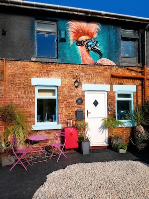 A building with a mural, a white door, and a red suitcase on the ground.
