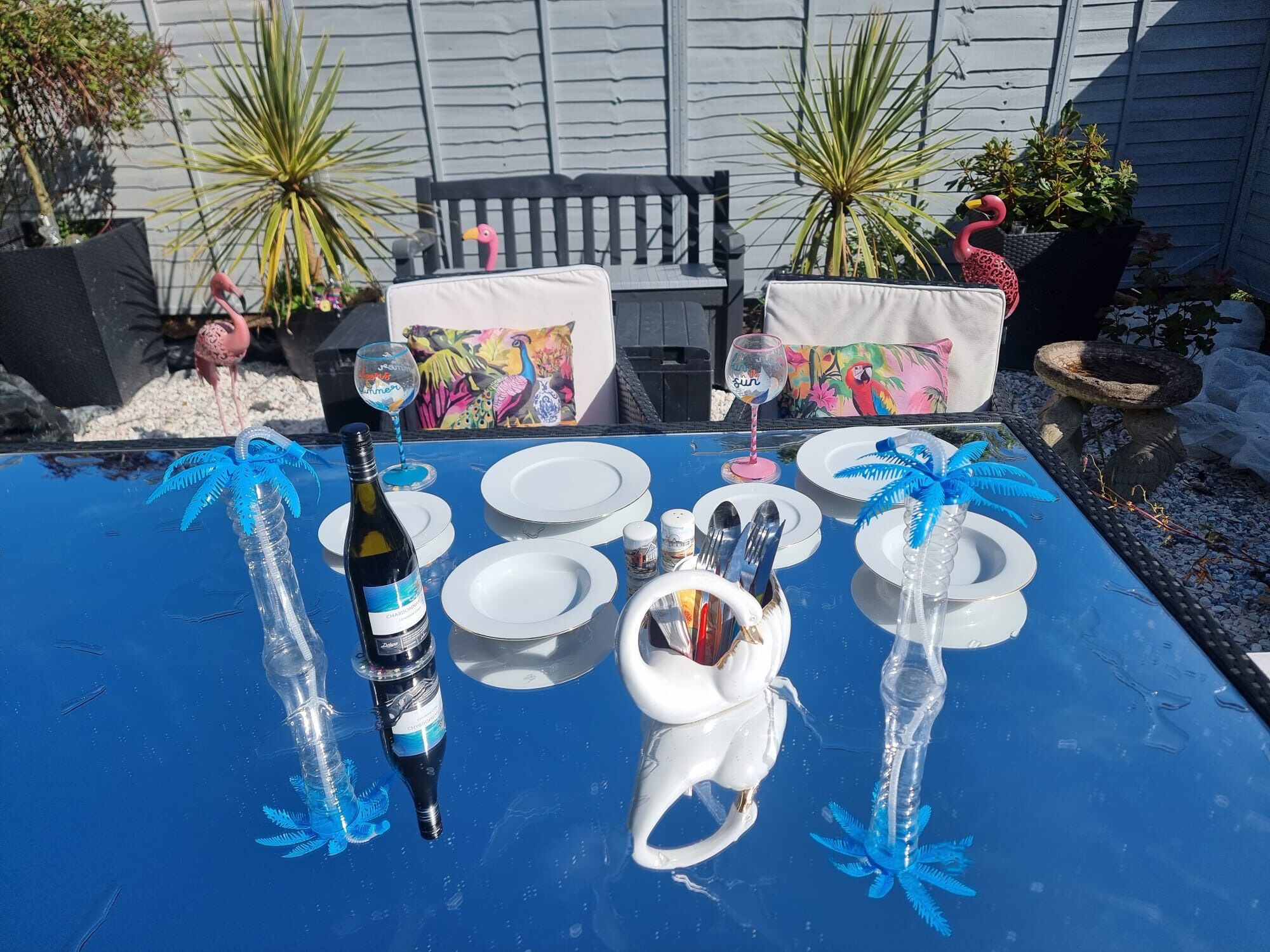 A dining table set with plates, cutlery, and a bottle of wine, surrounded by chairs and decorative pillows.