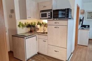 Eine kompakte Küche mit Mikrowelle, Kaffeemaschine und kleinem Kühlschrank.