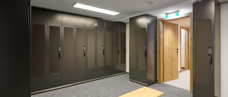 Un vestuario con varios armarios, un banco y una puerta que da a otra habitación.