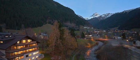 A multi-story hotel with balconies, a river, and a mountain range in the background.
