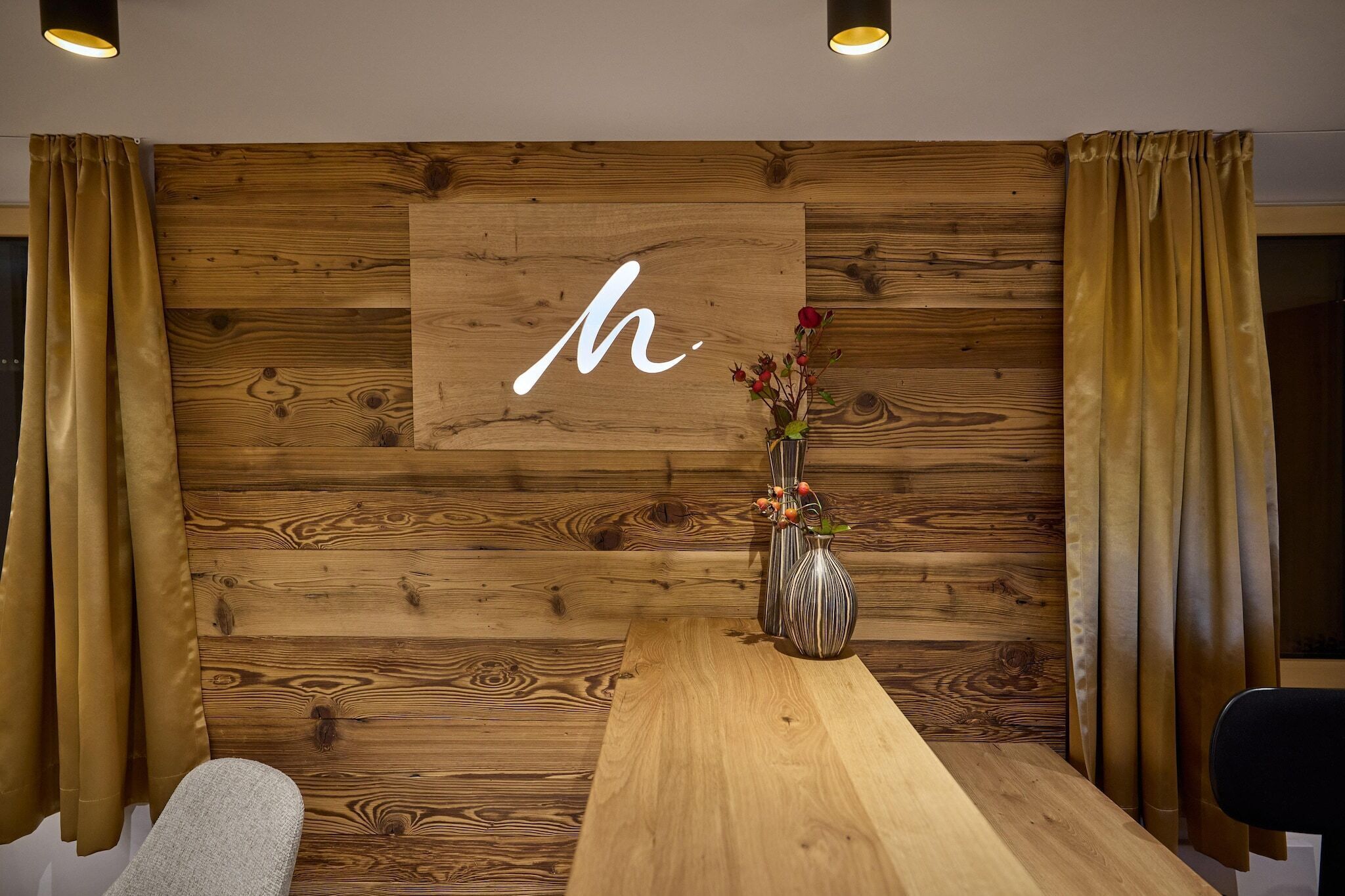 A reception area with a wooden wall, a large 'H' sign, a vase with flowers, and a wooden table.