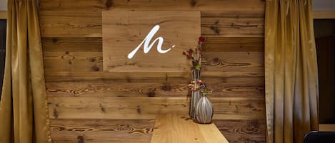 A reception area with a wooden wall, a large 'H' sign, a vase with flowers, and a wooden table.
