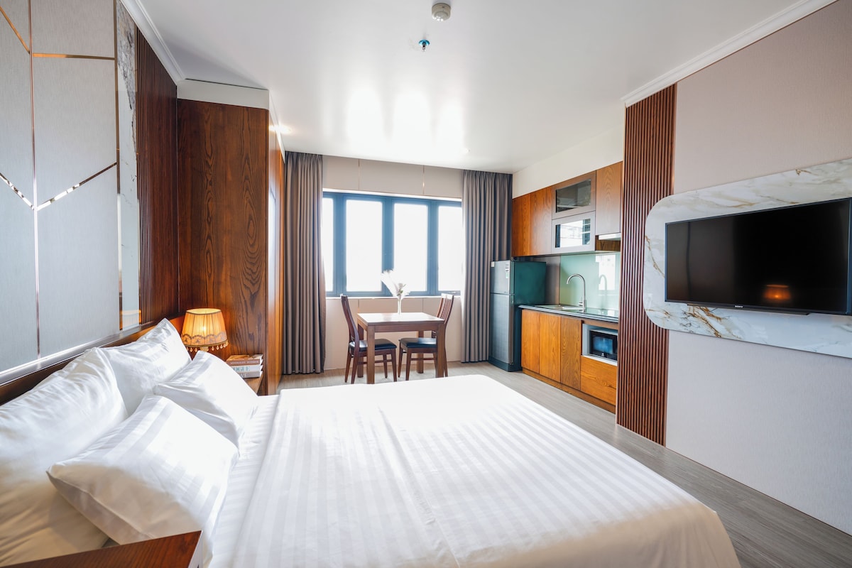 Quarto de hotel com uma cama grande, mesa de jantar, cozinha e televisão.