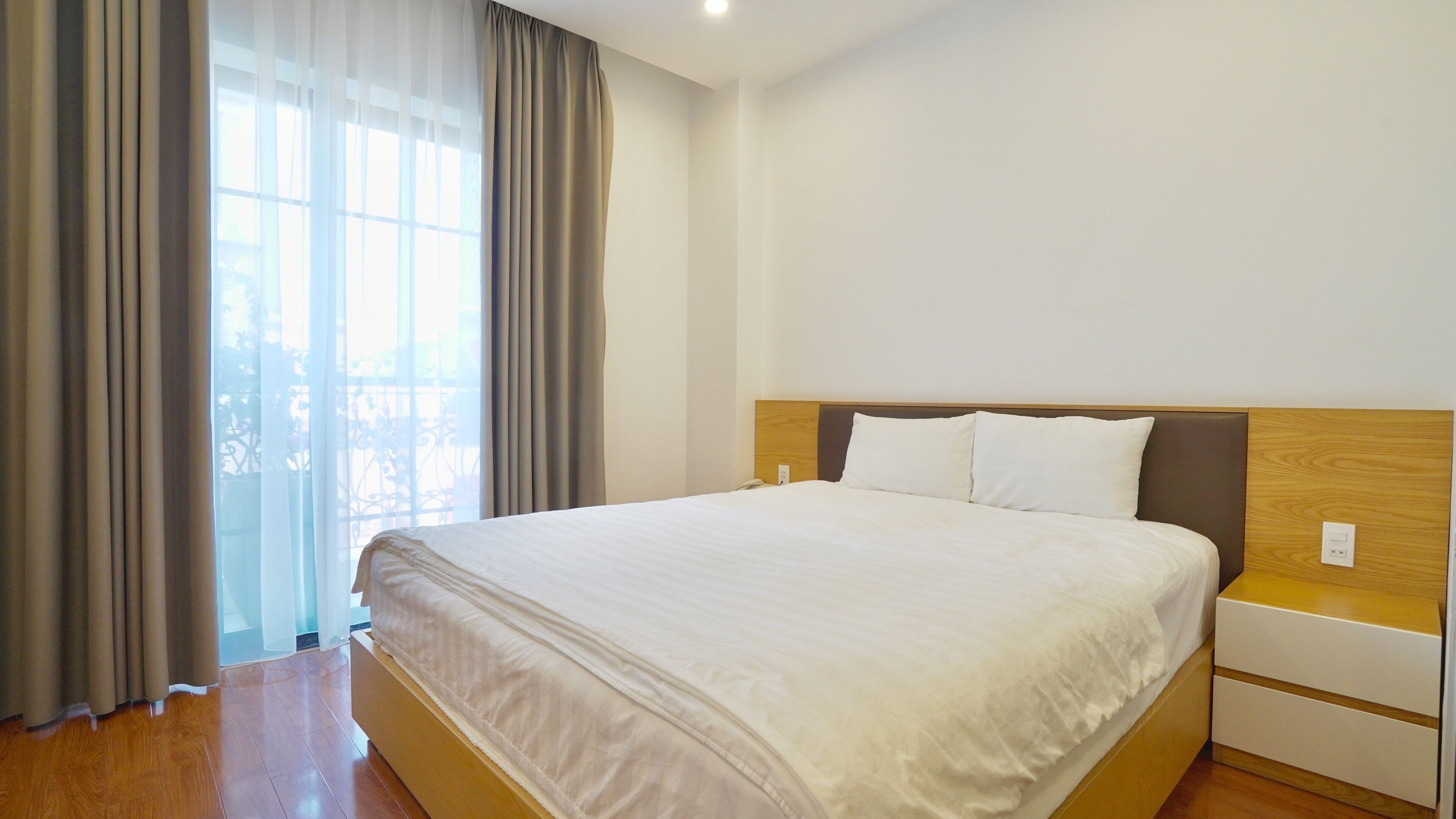 Una habitación de hotel con una cama grande, un cabecero de madera, una mesita de noche y una ventana con cortinas.