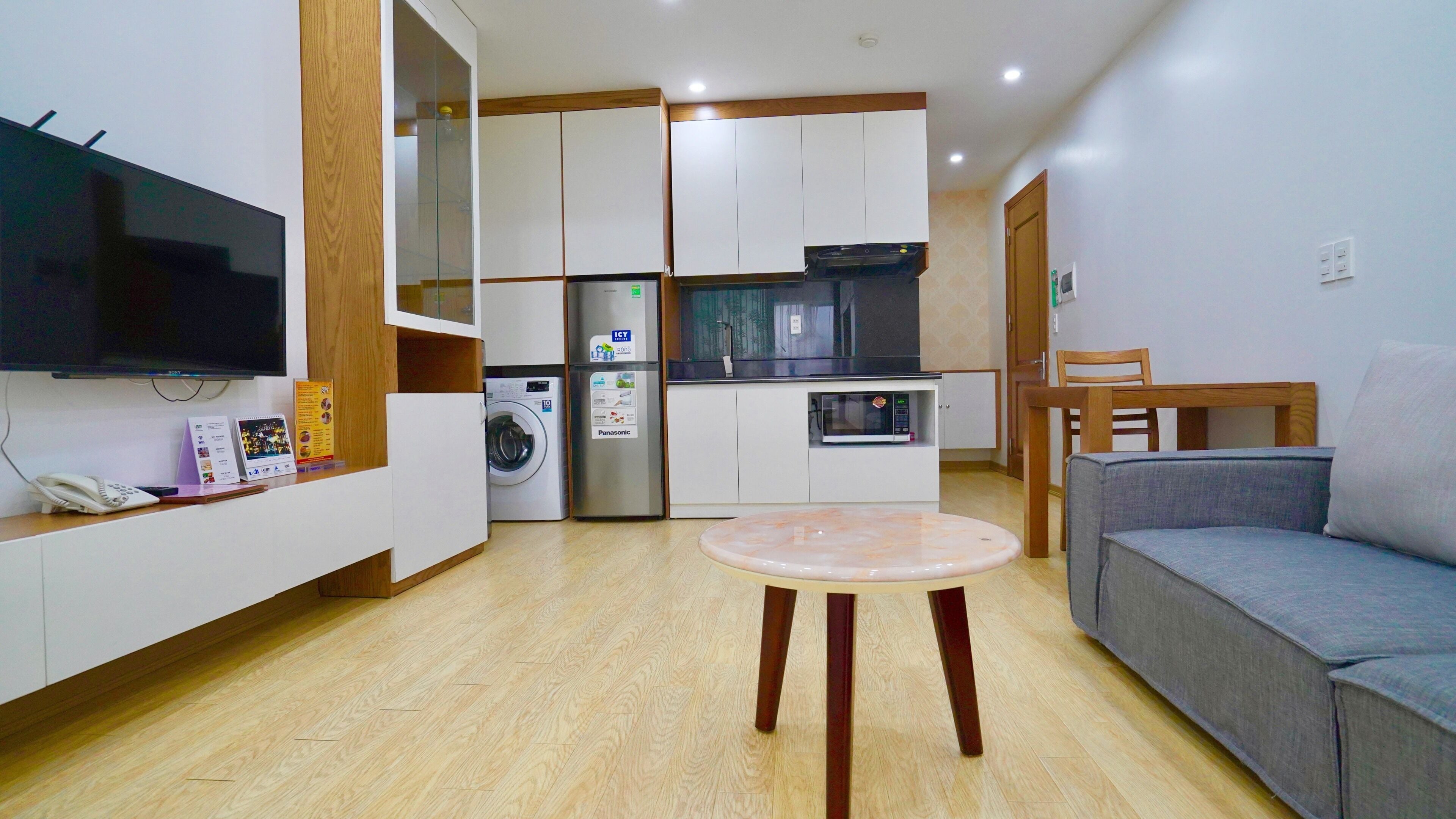 Un espacio habitable pequeño con sofá, una mesita, lavadora, microondas y televisor.