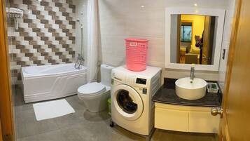 A compact bathroom with a bathtub, toilet, washing machine, and sink.