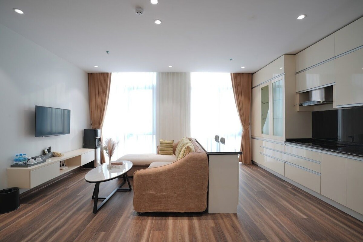 Quarto de hotel moderno com sofá, mesa de jantar, televisão de tela plana e cozinha compacta.