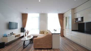 A modern hotel room with a sofa, a dining table, a flat-screen TV, and a kitchenette.