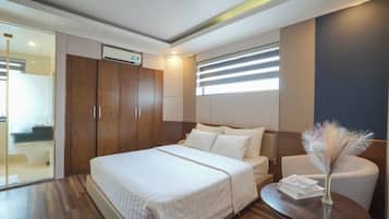 A hotel room with a large bed, a bedside table with a vase, and a wardrobe with a built-in air conditioning unit.