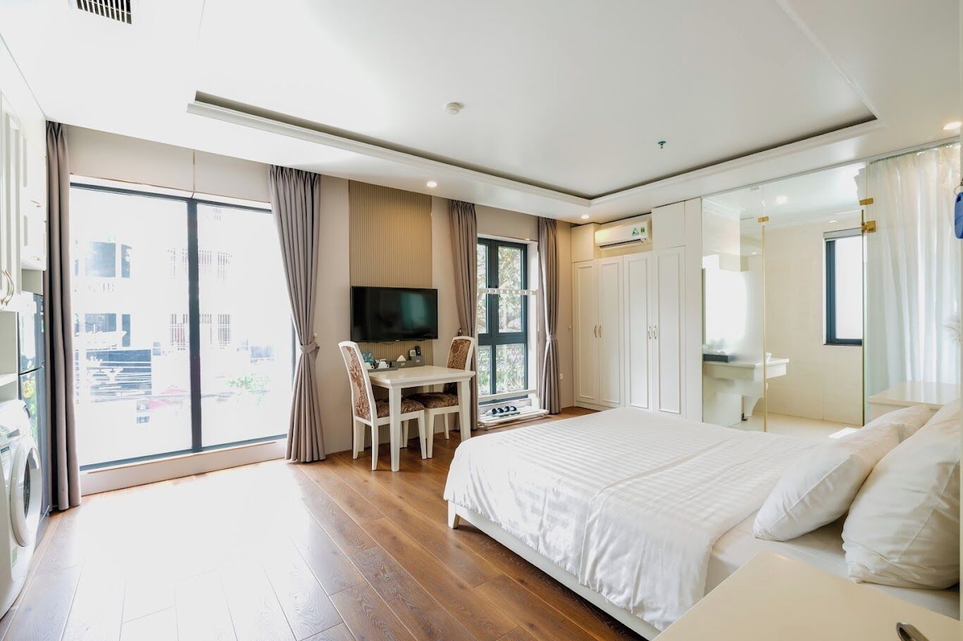 A hotel room with a large bed, a desk with chairs, a TV, and a sliding glass door to the outside.