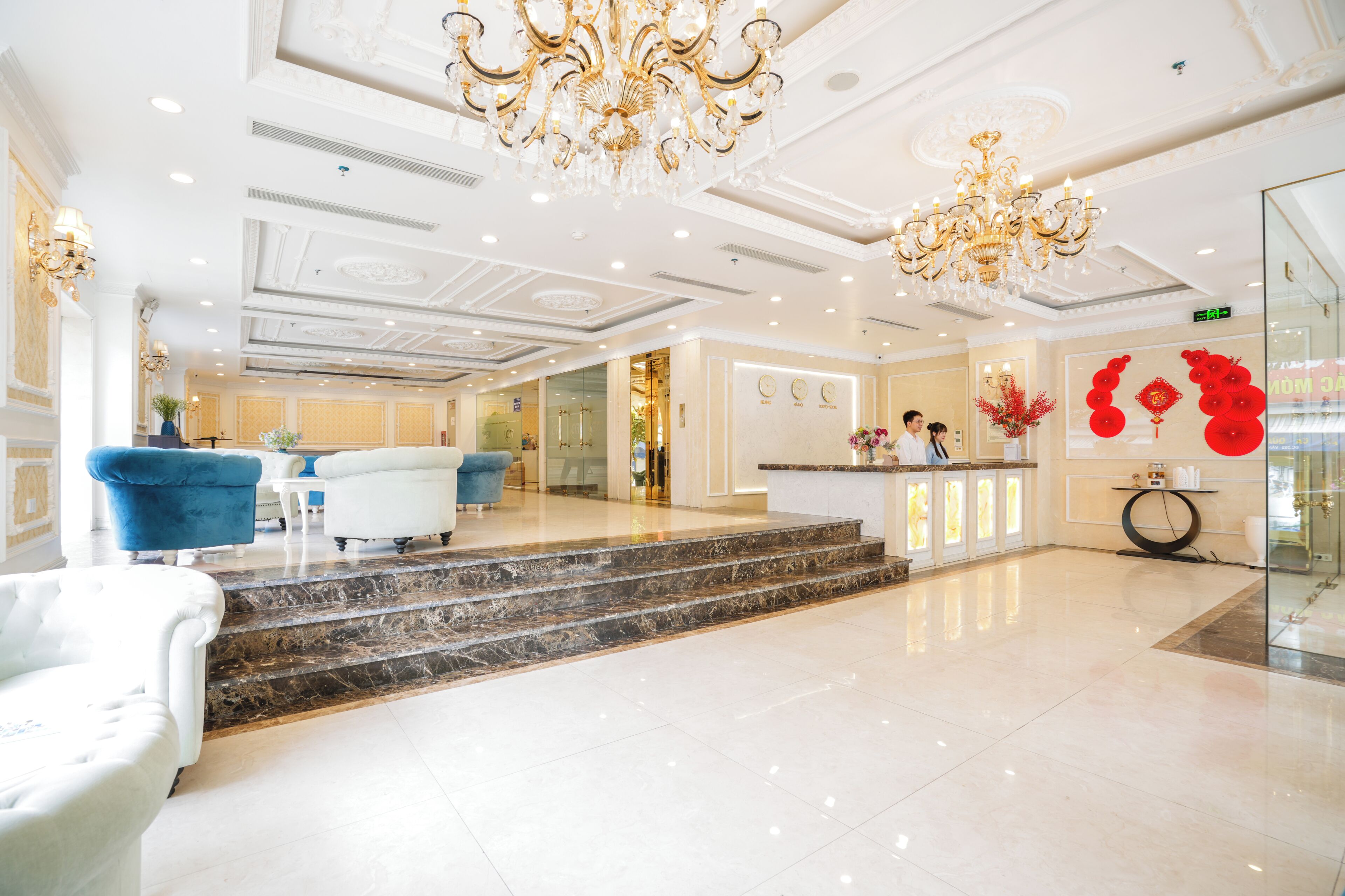 A hotel lobby with marble flooring, a reception desk, and a staircase leading to the upper floor.