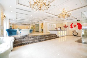 Un vestíbulo de hotel con piso de mármol, una mesa de recepción y una escalera que conduce al piso superior.