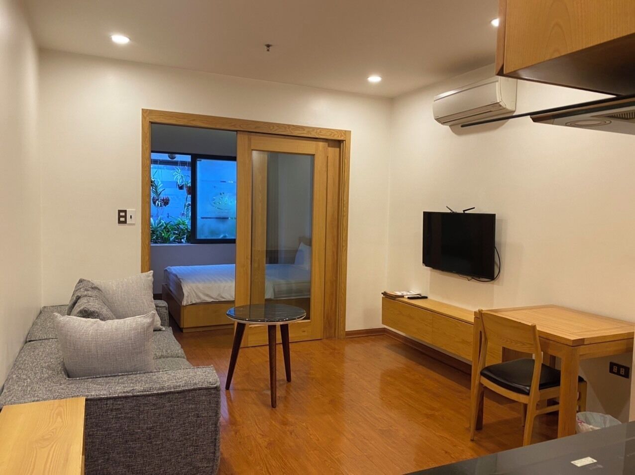 Un espacio habitable compacto con sofá, una mesita, televisor y puerta corredera que da a un balcón.