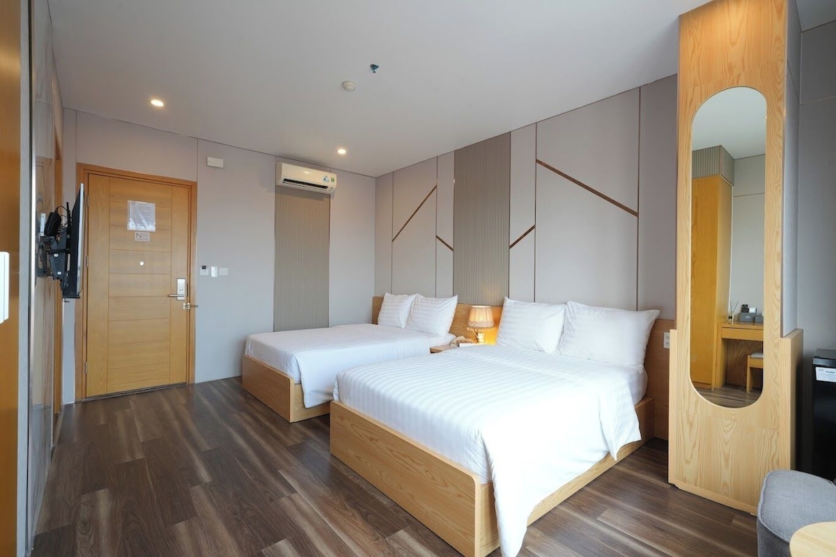 Quarto de hotel com duas camas, um guarda-roupa de madeira, um espelho e um ar condicionado.