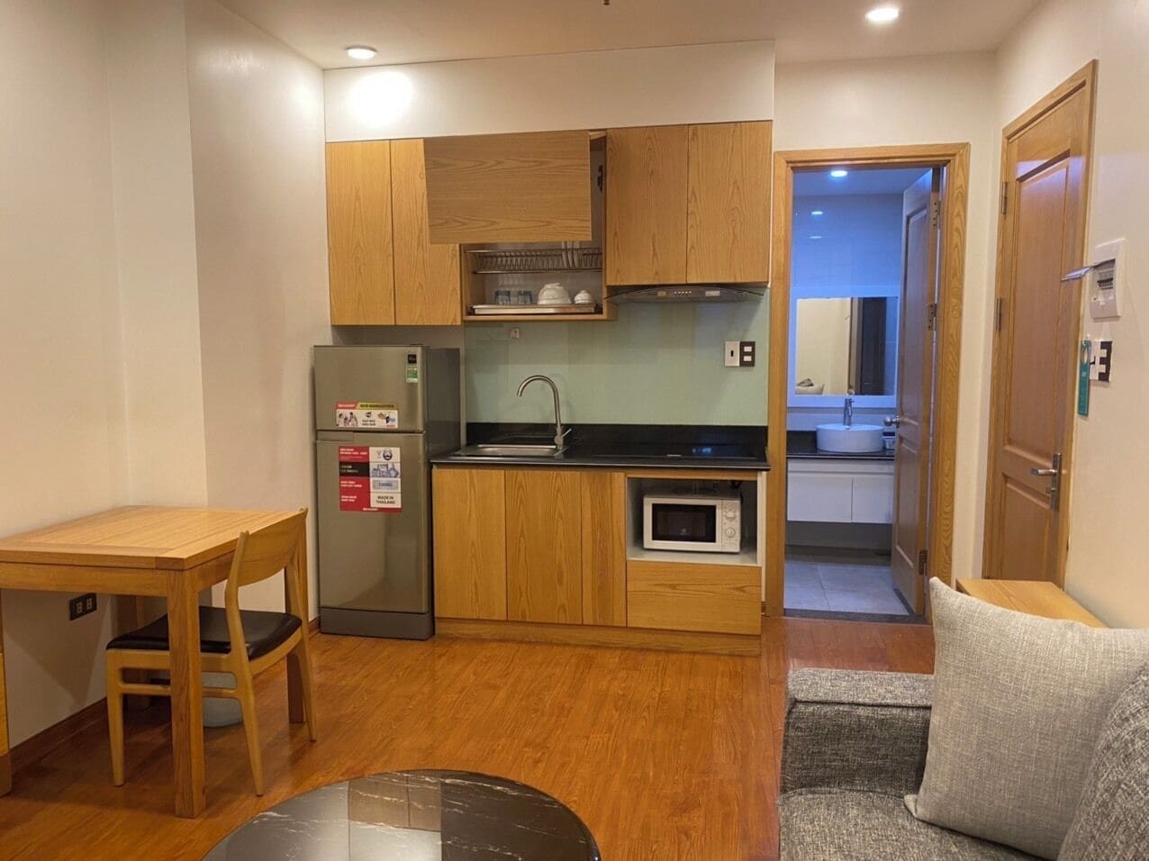 Una cocina compacta con armarios de madera, un refrigerador, un microondas y un lavamanos.
