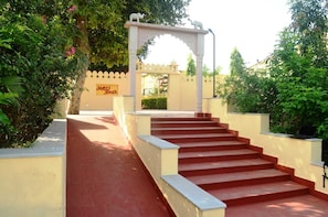 Un escalier rouge mène à une arche blanche surmontée d’une statue, le tout étant entouré de verdure et d’un bâtiment sur lequel on peut lire l’inscription « Meri Bagh ».