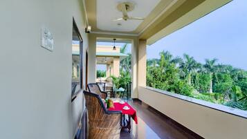 A balcony with wicker furniture, a red tablecloth, and a view of greenery.
