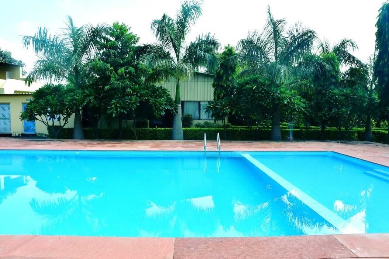 A swimming pool with clear blue water, surrounded by lush greenery and a building in the background.