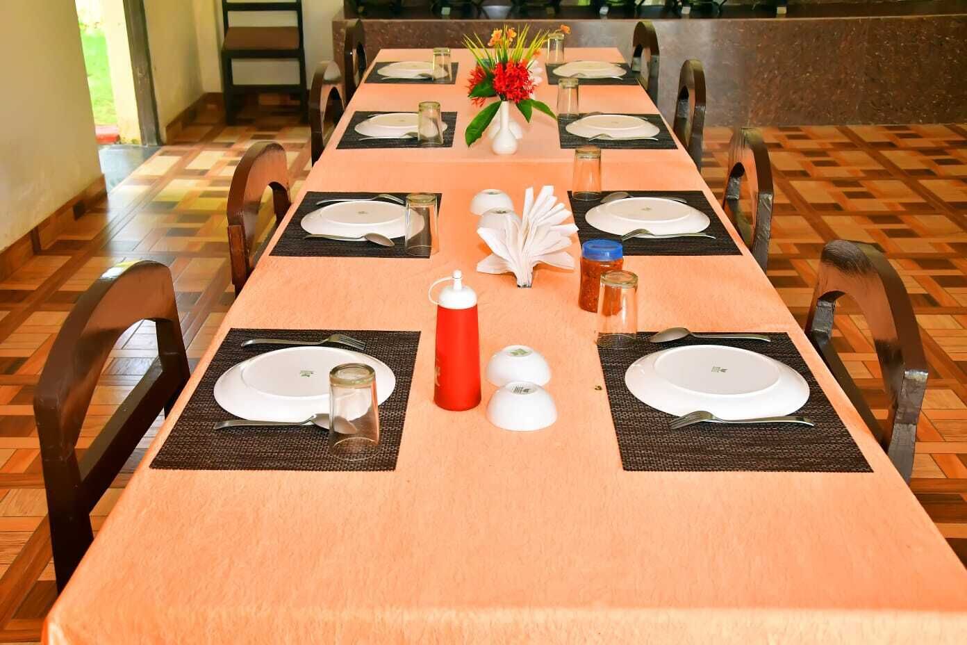 A dining table set with plates, cutlery, and condiments, with chairs around it.