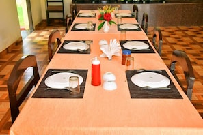 Une table à manger dressée avec des assiettes, des couverts et des condiments, entourée de chaises.