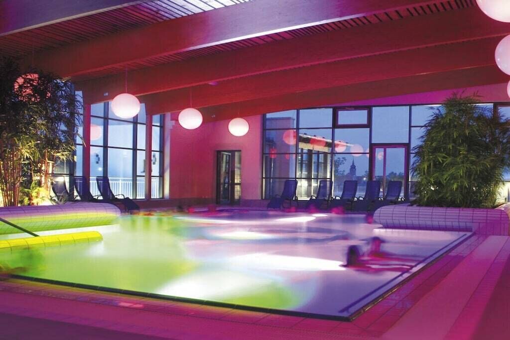 An indoor swimming pool with a glass barrier, lounge chairs, and a view of the outside.