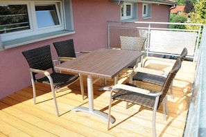 Une terrasse extérieure avec une table en bois et quatre chaises, une rambarde et un bâtiment en arrière-plan.