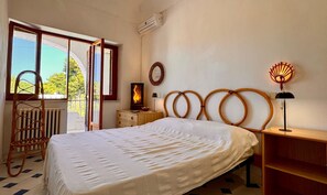 Ein Schlafzimmer mit Bett, Nachttisch, Lampe, Spiegel und Blick ins Freie.