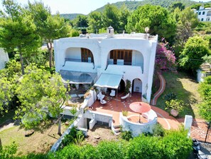 Eine weiße Villa mit Terrasse, Gartenmöbeln und einer Sitzgruppe.