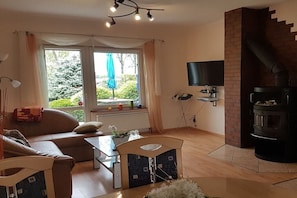 A living room with a sofa, a dining table, chairs, a fireplace, and a TV mounted on the wall.