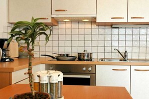 A kitchen with white cabinets, a tiled backsplash, a stove, a sink, and a potted plant. - Chardonnay - Santlhof (Kurtatsch)