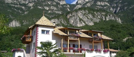 Un edificio de dos pisos con balcón, rodeado de vegetación y montañas.
