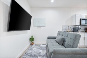 A modern living room with a grey sofa, a flat-screen TV mounted on the wall, a small plant, and a patterned rug. - Chic 1-Bedroom Retreat - Phoenix (Phoenix)