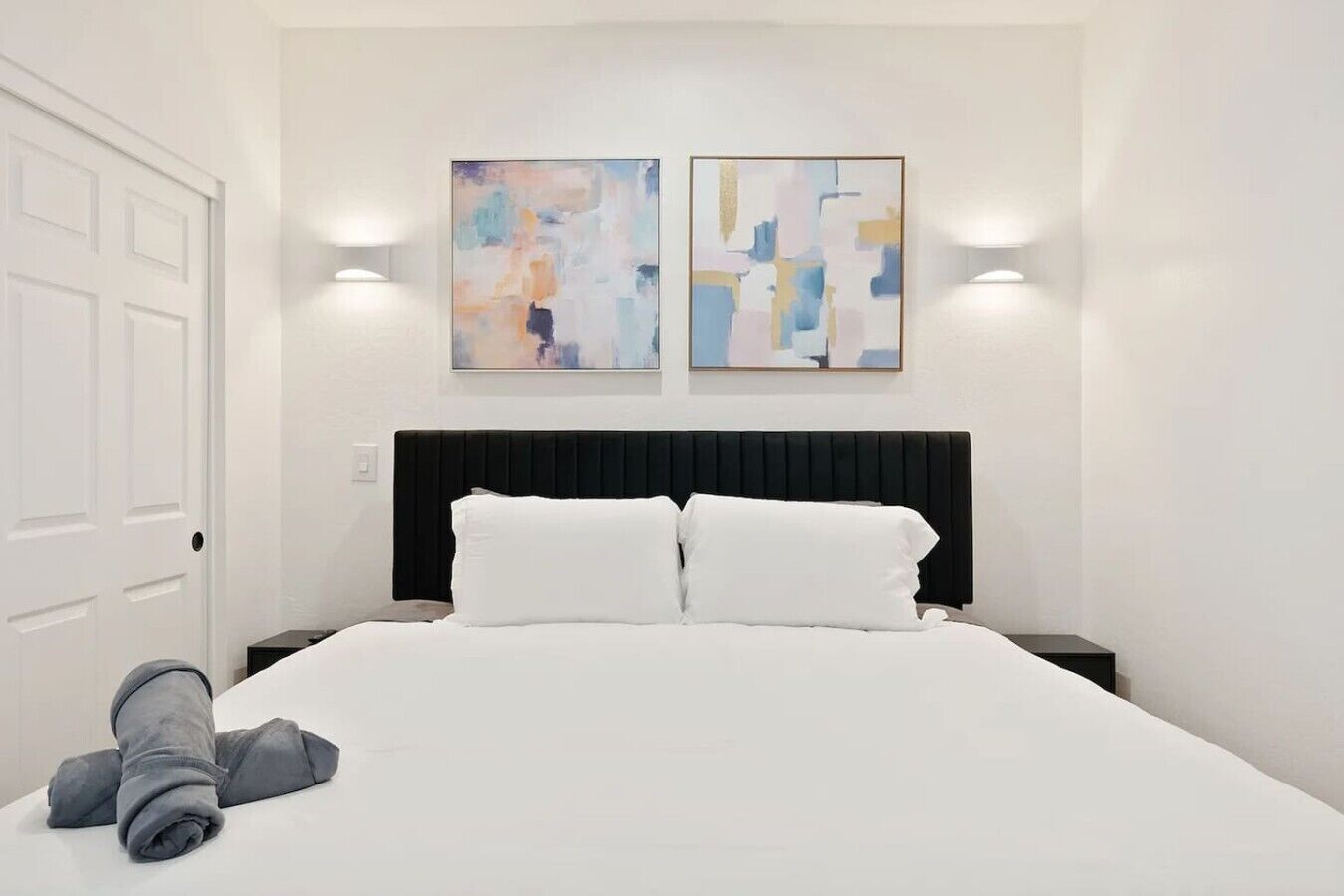 A hotel room with a bed, two wall-mounted light fixtures, and abstract art on the wall.