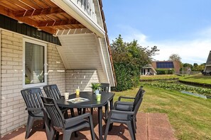 An outdoor patio with a table and chairs, a brick wall, and a solar panel on a building in the background. - Holiday apartment with 3 bedrooms (Gramsbergen)