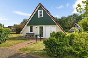 A single-story house with a green roof, white walls, and a front door. There is a bench and a small table outside. - Holiday apartment with 3 bedrooms (Gramsbergen)