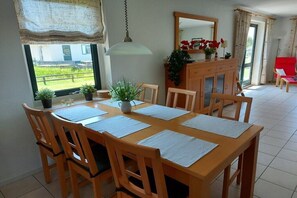 A dining area with a wooden table and chairs, a cabinet with a mirror, and a view of greenery outside. - Villaparc Duynopgangh House 28 (Julianadorp aan Zee)