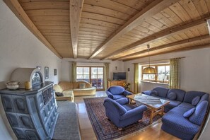 Ein geräumiges Wohnzimmer mit hoher Holzbalkendecke, einer Sofagarnitur, einem Fernseher und einem Kamin.