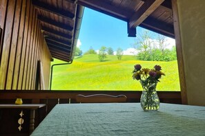 A room with a table and a vase of flowers, a window with a view of a green field and trees. - Lauchlehen - Fewo Göll (Bischofswiesen)