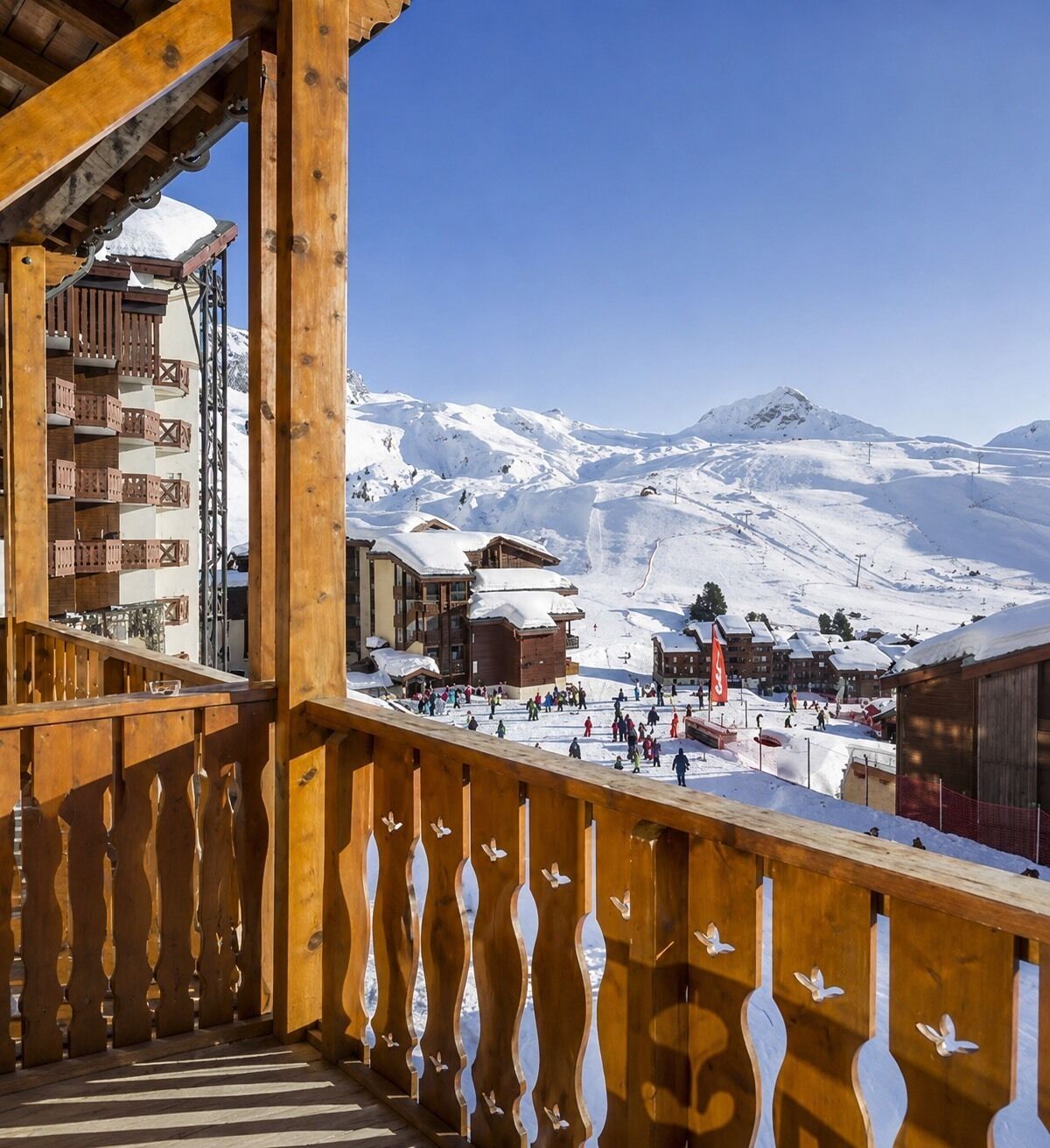 Un balcón de madera con vistas a un complejo turístico nevado, con edificios y pistas de esquí.