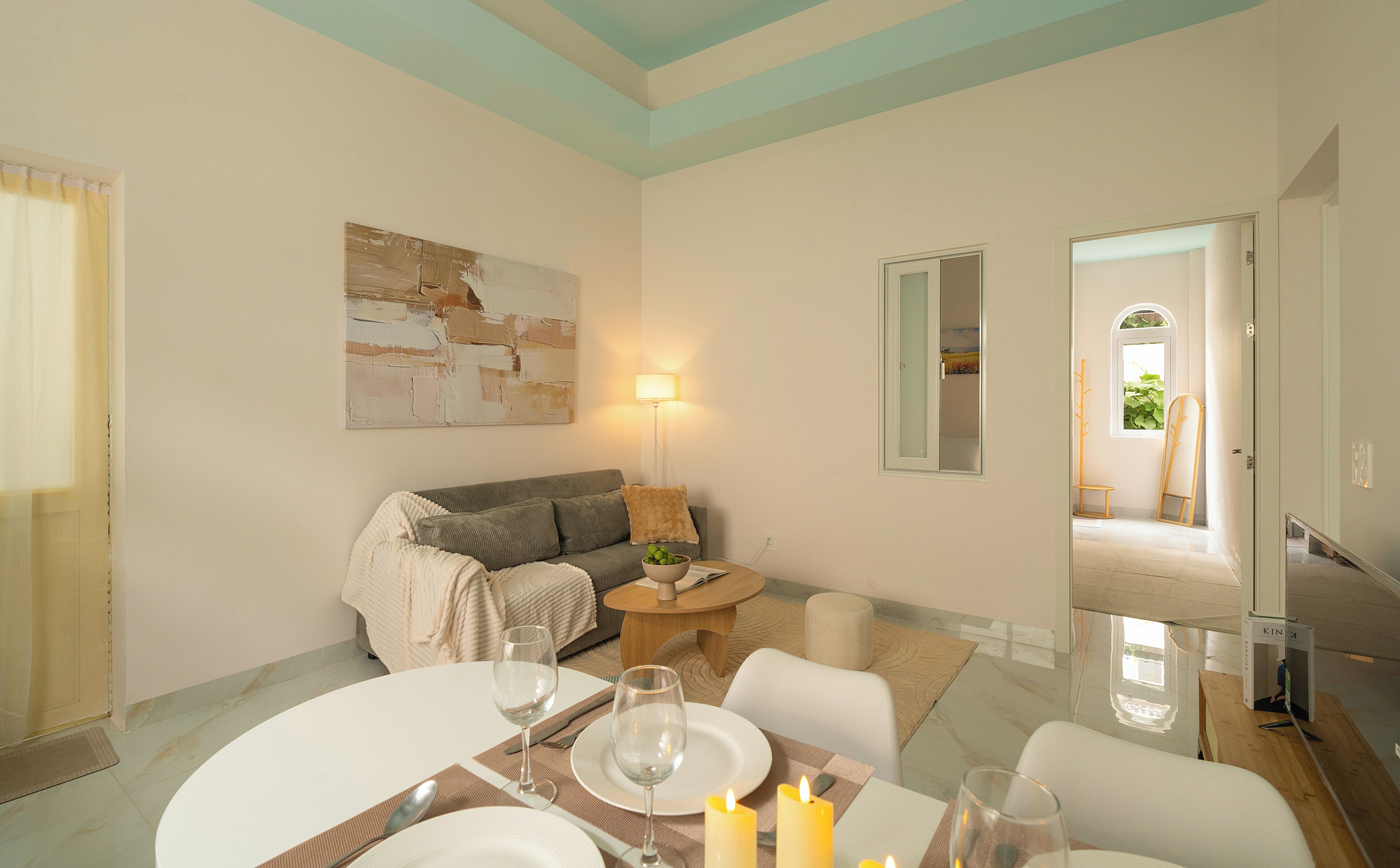 Un salon avec un canapé, une table à manger dressée pour deux personnes, un tableau au mur et une lampe.