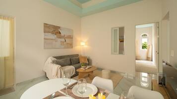 Un salon avec un canapé, une table à manger dressée pour deux personnes, un tableau au mur et une lampe.