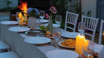 Une table à manger dressée avec des assiettes, des verres et des bougies, entourée de chaises blanches.