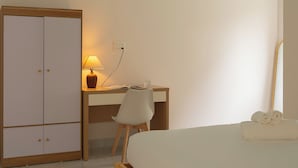A bedroom with a bed, a desk with a chair, a wardrobe, and a lamp.