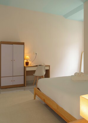 Een slaapkamer met een bed, bureau met stoel, kledingkast en lamp.