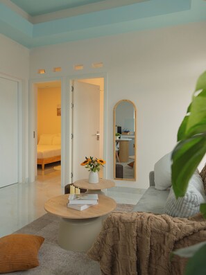 A modern living room with a round coffee table, a sofa, a mirror, and a door leading to a bedroom.