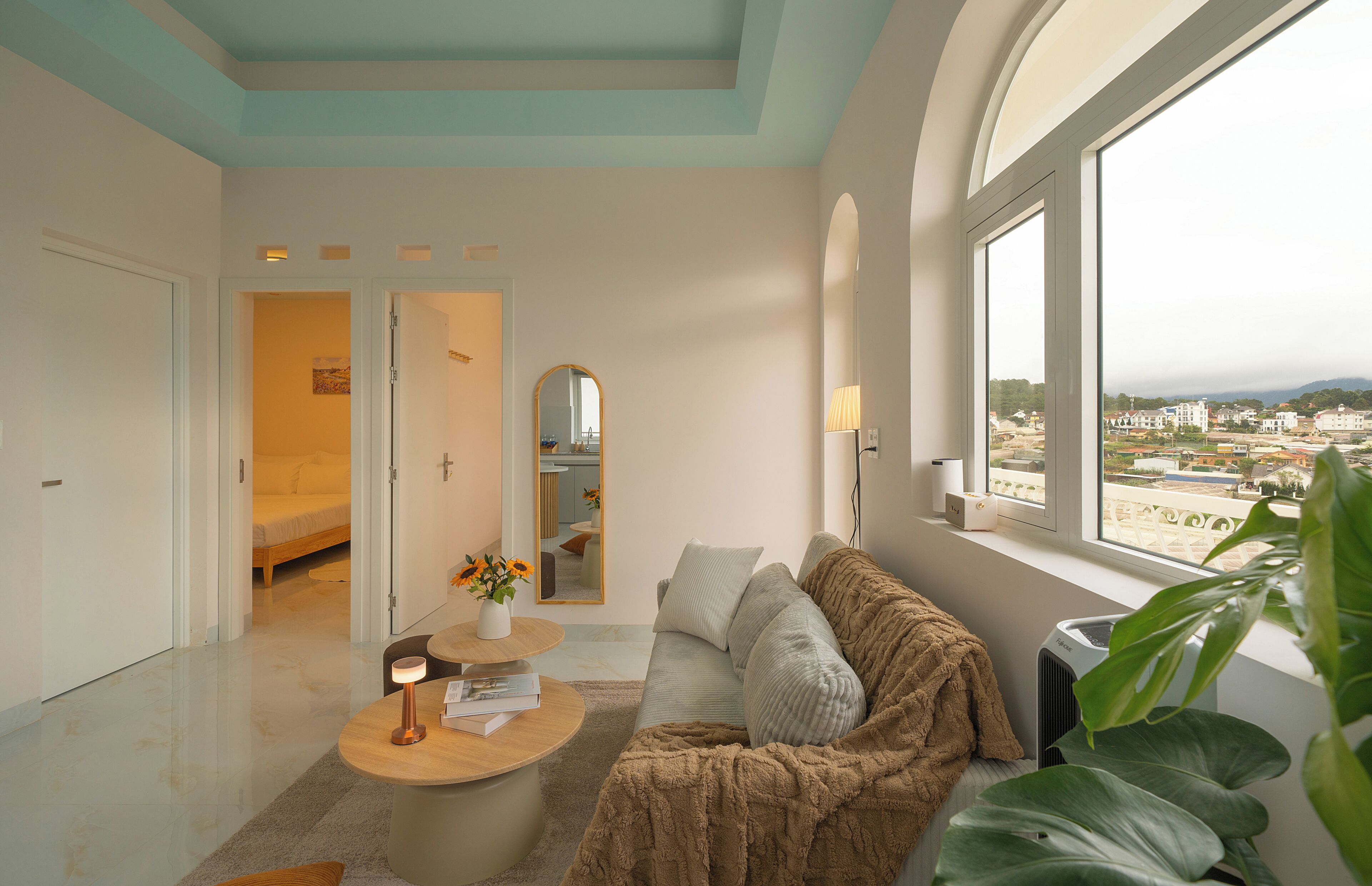 A modern living room with a sofa, a coffee table, and a view of a cityscape through large windows.