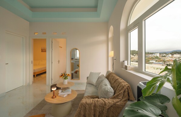 A modern living room with a sofa, a coffee table, and a view of a cityscape through large windows.